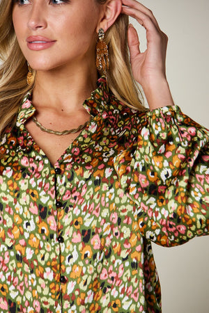 Model wearing a vibrant, floral patterned blouse with frill detailing and bloused sleeves.