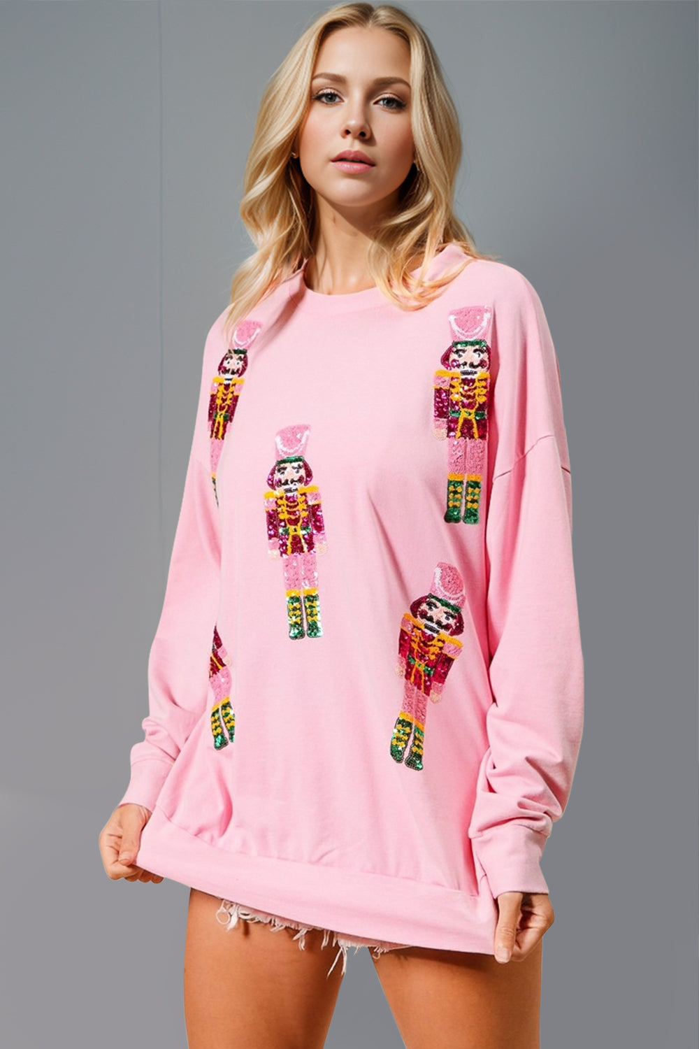 Model wearing a pink long sleeve sweatshirt featuring colorful sequin nutcracker designs.