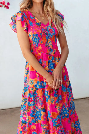 Woman in a boho floral V-neck ruffle tiered dress, featuring vibrant pink and blue patterns.