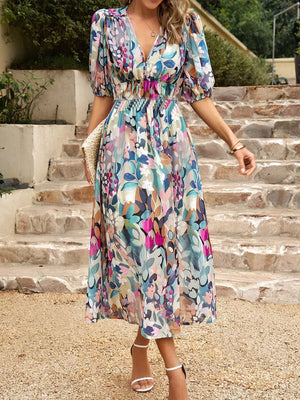 Model wearing a colorful printed puff sleeve midi dress with a cinched waist, walking on a stone pathway.
