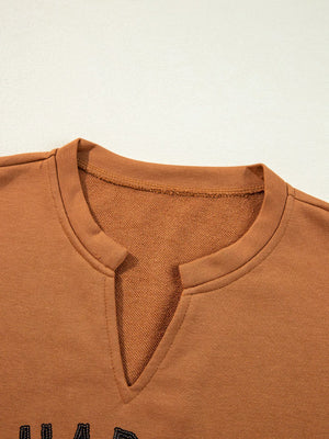 Close-up of the notched neckline of a Happy Halloween graphic long sleeve top in orange.