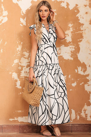 Ruffled printed surplice cap sleeve dress with bold black and white pattern, paired with woven bag against textured wall.