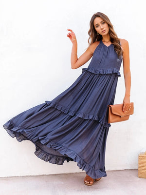 Model in a navy ruffled sleeveless tiered maxi dress with pockets, styled with a clutch and sandals.