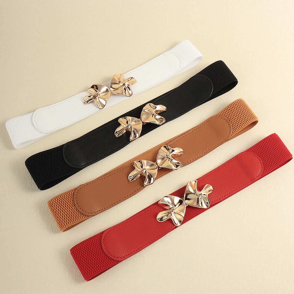 Four colorful elastic belts with alloy buckles in white, black, brown, and red on a neutral background.