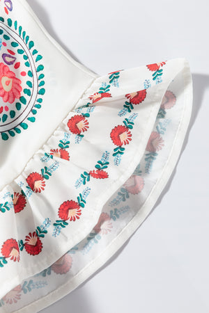 Detail of a floral print blouse featuring intricate embroidery and ruffle trim in vibrant colors on a white background.