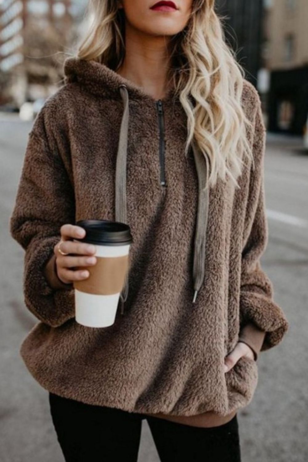 Woman in a cozy quarter-zip drawstring teddy hoodie holding a coffee cup on a city street.