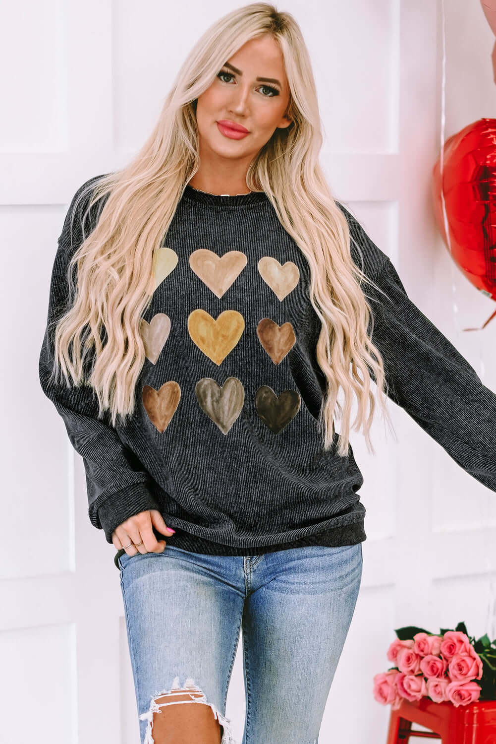 Woman wearing a heart-printed round neck dropped shoulder sweatshirt, paired with distressed jeans.