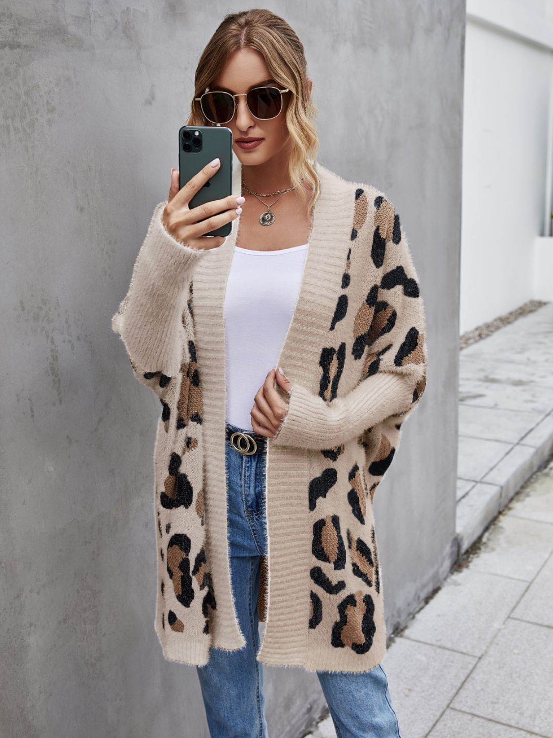 Woman wearing an open front leopard pattern fuzzy cardigan, styled casually with sunglasses and a white top.