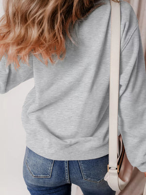 Back view of a woman wearing a gray Halloween ghost sweatshirt, paired with jeans and a stylish bag.