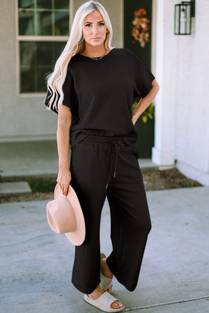 Model wearing a black double take full size texture short sleeve top and pants set with a pink hat.