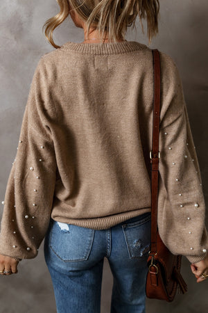 Back view of a pearl detail round neck long sleeve sweater in beige, paired with blue jeans and a brown bag.