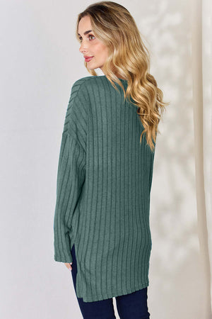 Back view of a model wearing a ribbed green high-low T-shirt with long sleeves.
