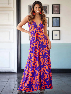 Model wearing a vibrant orange and purple twisted printed V-neck cami maxi dress in a stylish interior setting.