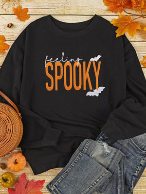 Feeling Spooky Halloween embroidered sweatshirt in black with orange text and bats, styled with denim and autumn leaves.