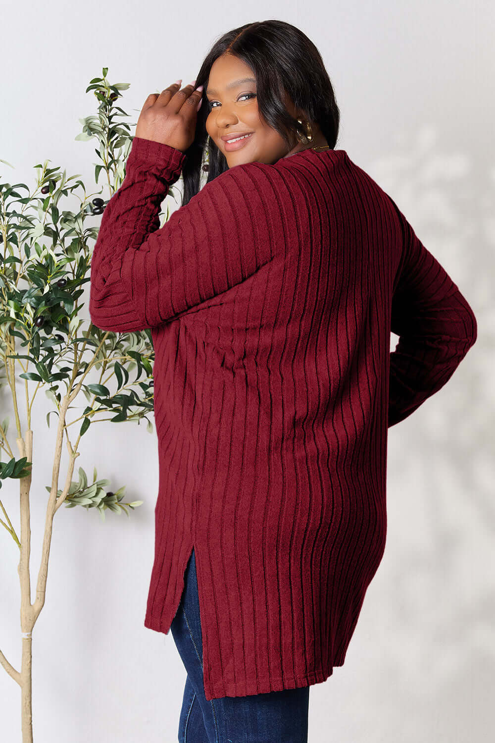 Plus size model wearing a burgundy ribbed long sleeve top with a high-low slit design, showcasing a stylish back view.