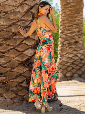 Model wearing a vibrant floral Twisted Printed V-Neck Cami Dress, posing against a palm tree backdrop.