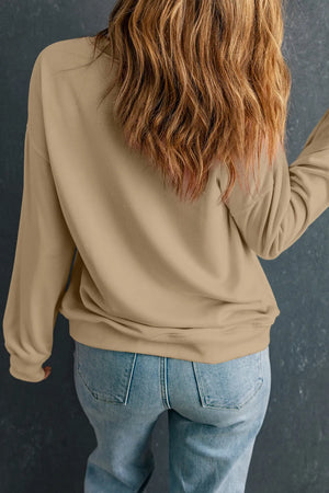 Model wearing a beige long sleeve sweatshirt with blonde hair, paired with light blue jeans, showcasing a casual style.