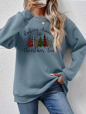 Model wearing a blue Christmas sweatshirt with 'Rocking Around the Christmas Tree' graphic and colorful trees.
