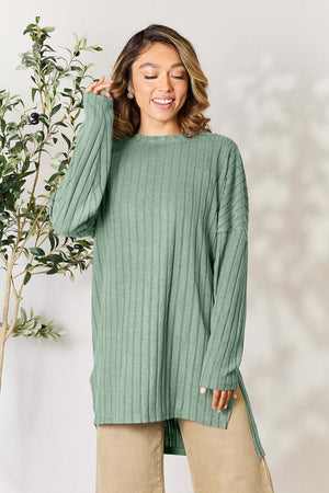 Model wearing a light green ribbed long sleeve slit top with a high-low design, styled casually with neutral pants.
