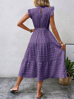 Back view of a woman wearing a lavender tied ruffled cap sleeve midi dress, featuring a tiered skirt and belted waist.