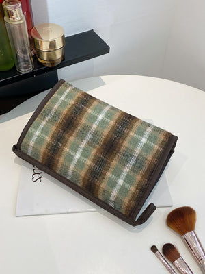 Contrast plaid clutch bag with zipper in green and brown tones on a table, perfect for stylish storage.