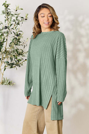 Model wearing a green ribbed long sleeve top with a round neck and side slits, paired with beige pants.