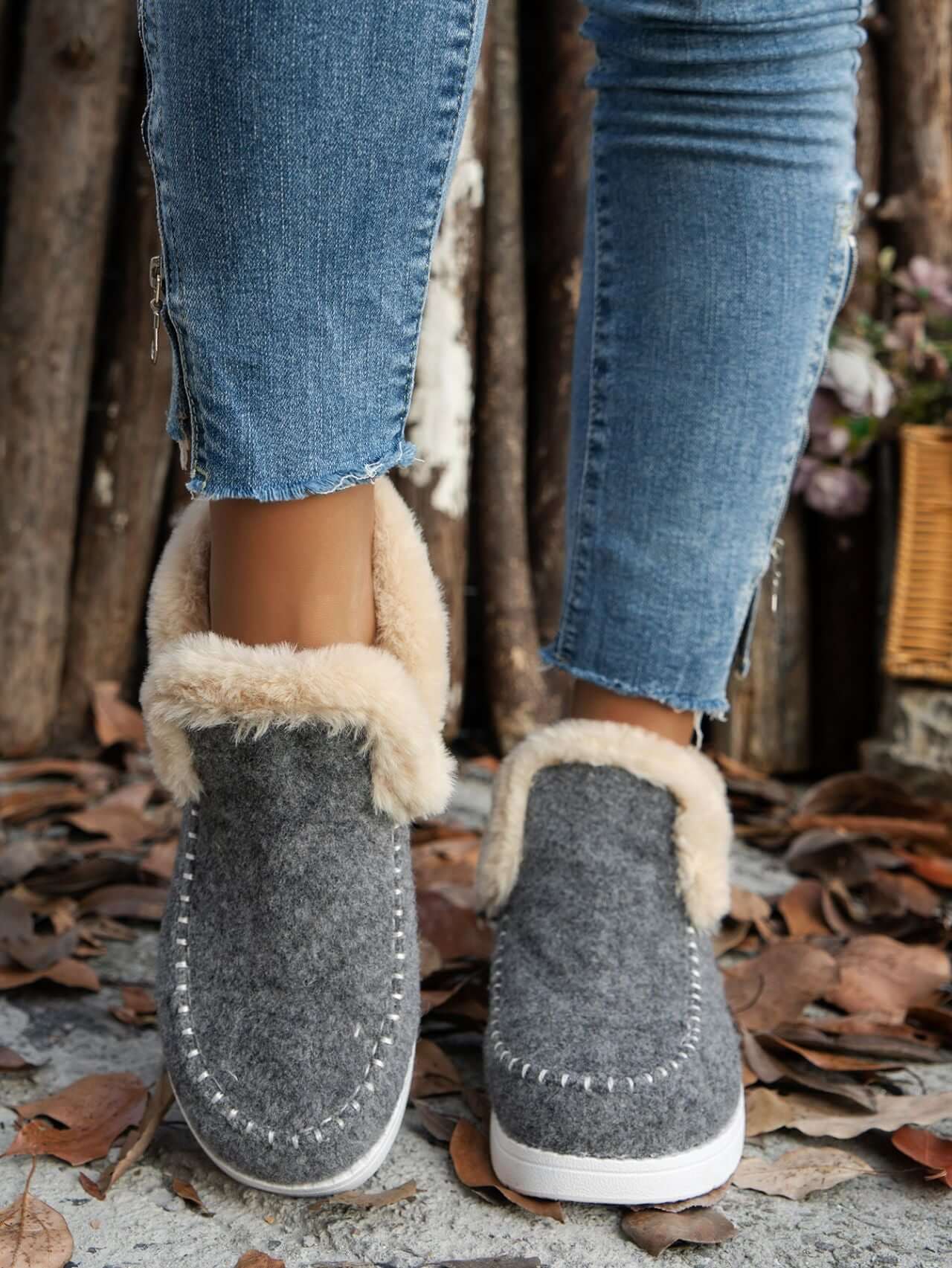 Furry suede round toe flat sneakers with fur-lined soles, styled with denim jeans among autumn leaves.