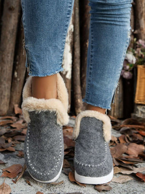 Furry suede round toe flat sneakers with fur-lined soles, styled with denim jeans among autumn leaves.