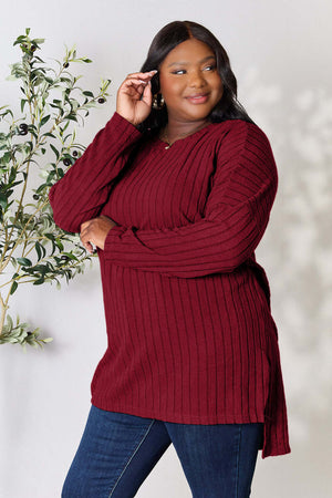 Plus-size model wearing a burgundy ribbed long sleeve slit top, styled with jeans and smiling, showcasing a casual look.