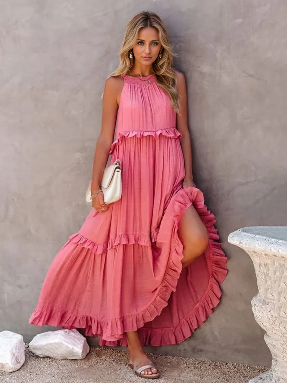 Ruffled sleeveless tiered maxi dress in pink with pockets, styled on a model against a textured wall.