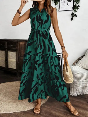 Printed tie waist sleeveless maxi dress in green with leaf print, styled with a casual woven bag and sandals.