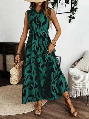 Woman wearing a printed tie waist sleeveless maxi dress with leafy patterns in green, perfect for stylish summer outings.