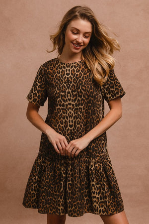 Chic woman wearing a leopard print tie back round neck short sleeve dress with a flared skirt against a neutral background.