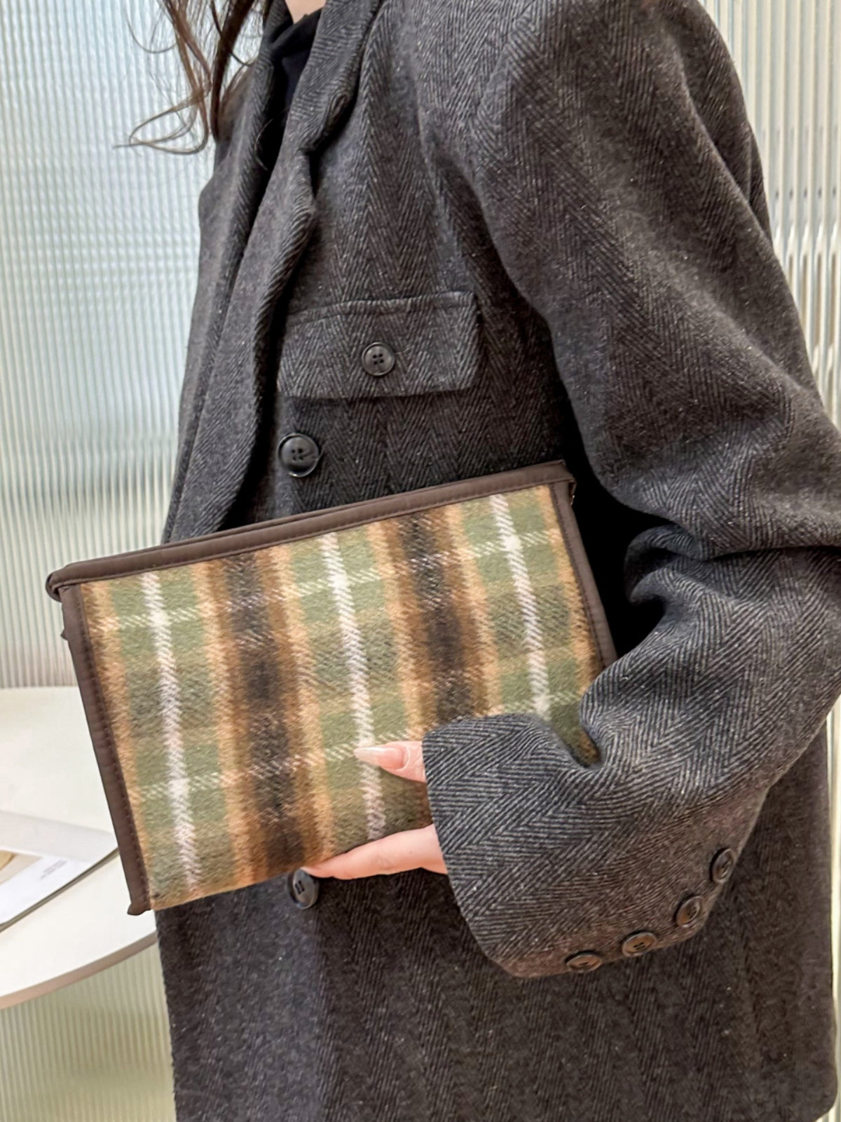 Contrast plaid clutch with zipper held by a person in a stylish gray coat, perfect for adding elegance to any outfit.