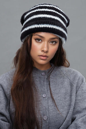 Model wearing a fuzzy contrast striped thermal hat in black and white, paired with a grey sweater, showcasing a stylish winter look.