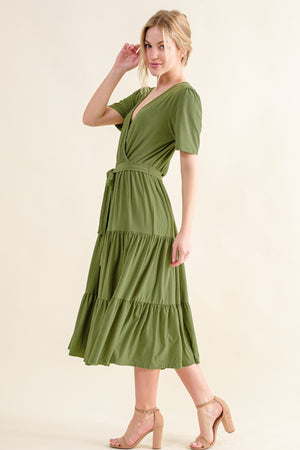 Woman wearing a chic olive green short sleeve tiered midi dress, featuring a flattering wrap design.