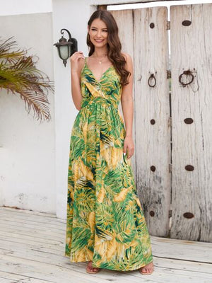 Beautiful woman in green and yellow printed surplice spaghetti strap dress standing on a wooden deck.