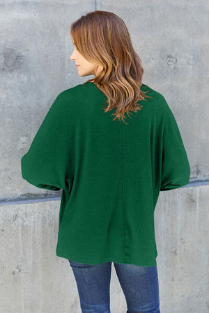 Woman from behind in a green oversized top against a grey backdrop, showcasing casual and stylish wear.