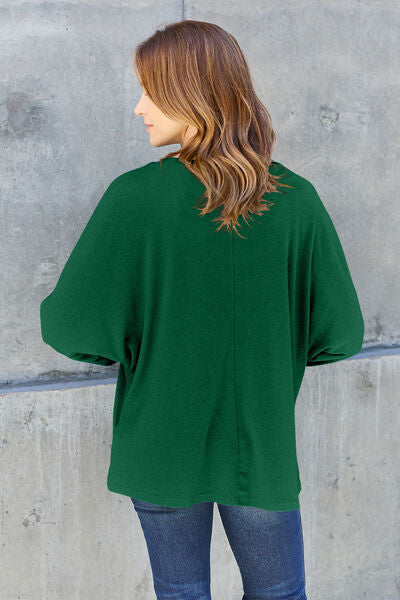 Woman from behind in a green oversized top against a grey backdrop, showcasing casual and stylish wear.