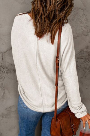 Back view of a woman in a light gray long sleeve top with a brown crossbody bag, casually styled with denim.
