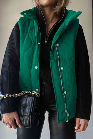 Model wearing a green collared neck vest with pockets over a black sweater, holding a chic handbag.
