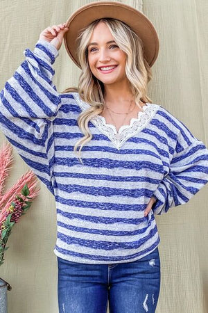 Chic striped lace detail V-neck top on model, showcasing stylish blue and white stripes with a fashionable hat.