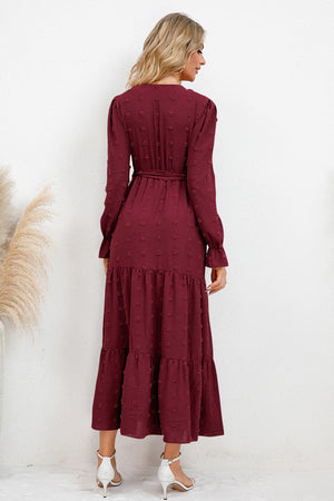 Back view of a woman wearing a burgundy Swiss dot tied surplice flounce sleeve dress, showcasing its flowing tiers.