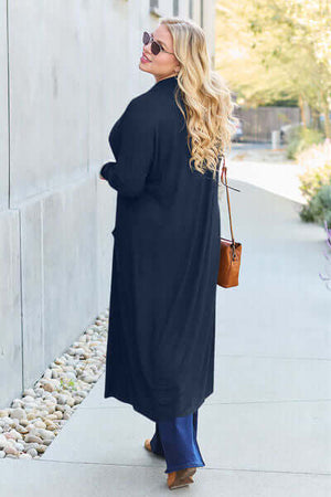 Back view of a woman wearing a Basic Bae open front long sleeve cover up in navy, strolling outdoors with a stylish handbag.