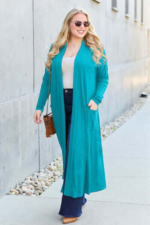 Woman wearing teal Basic Bae full size long sleeve cover-up with pockets, styled with sunglasses and denim.