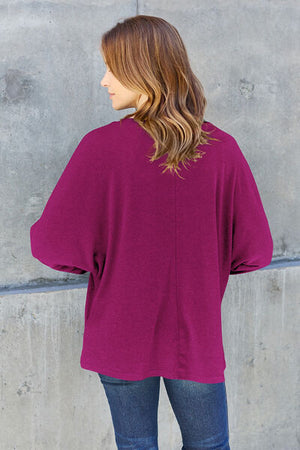 Model wearing a burgundy oversized top, showcasing the back design against a concrete background.