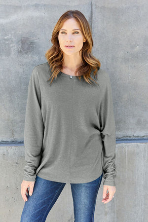 Model wearing a stylish grey round neck long sleeve t-shirt paired with jeans against a concrete background.