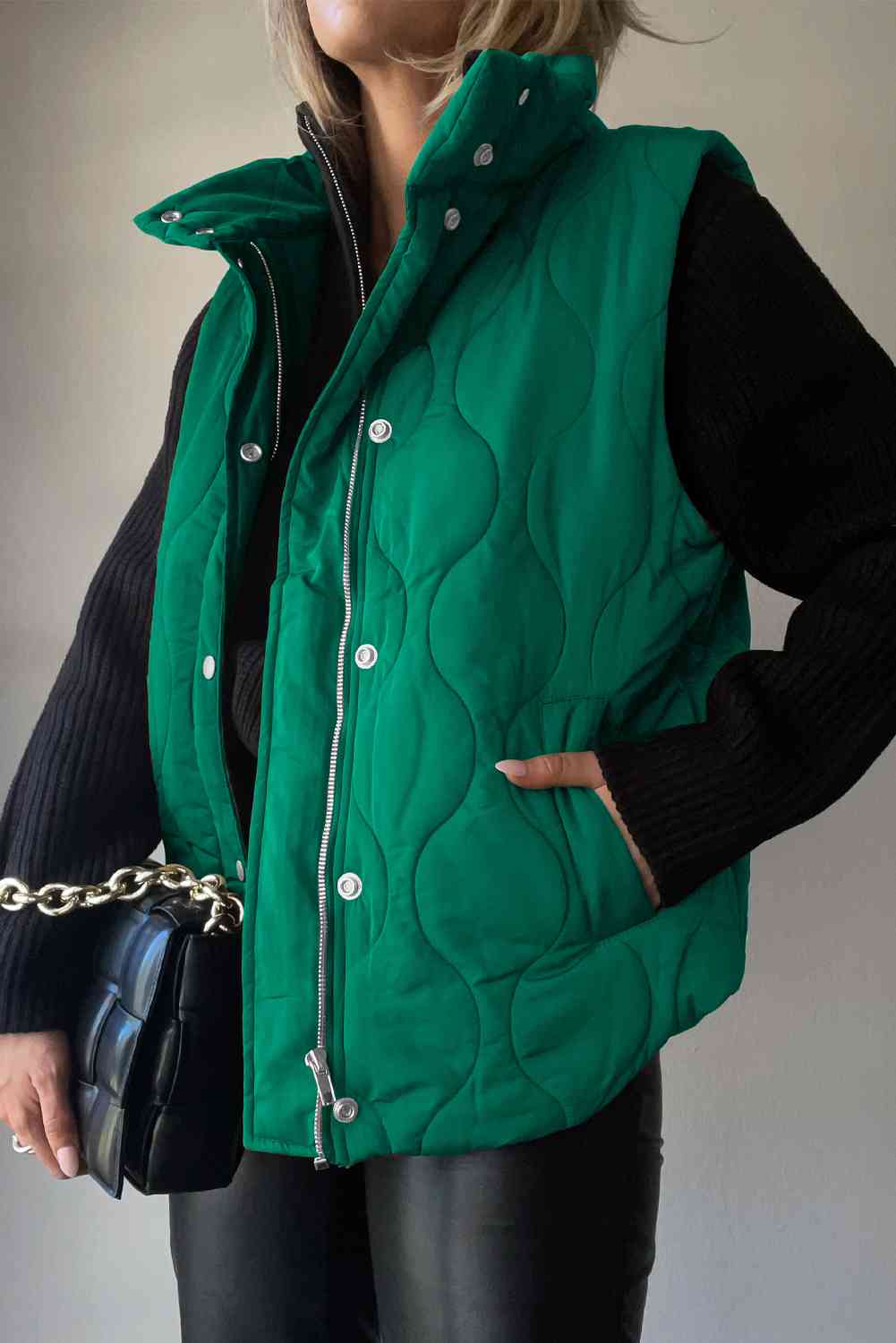 Collared green vest with pockets, featuring a quilted design and worn over a black sweater.