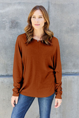 Model wearing a brown long sleeve t-shirt paired with jeans against a light concrete background.