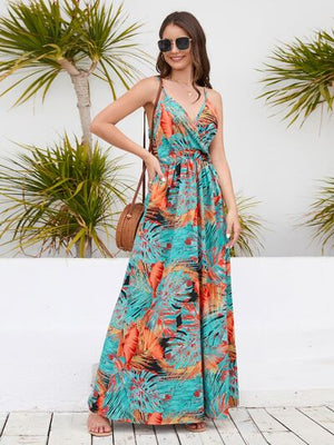 Model wearing a printed surplice spaghetti strap dress with tropical palm leaves against a beachside backdrop.